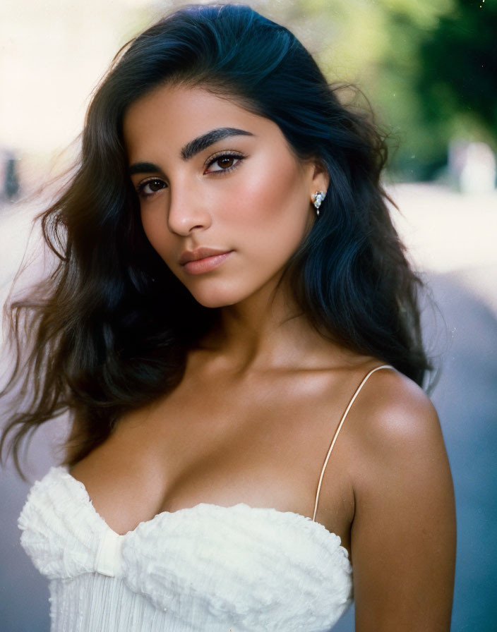 Portrait of woman with long, wavy dark hair in white top, gazing at camera