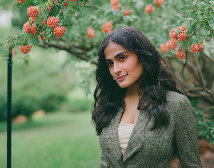 Woman in checkered blazer smiling by orange flower shrub in green garden