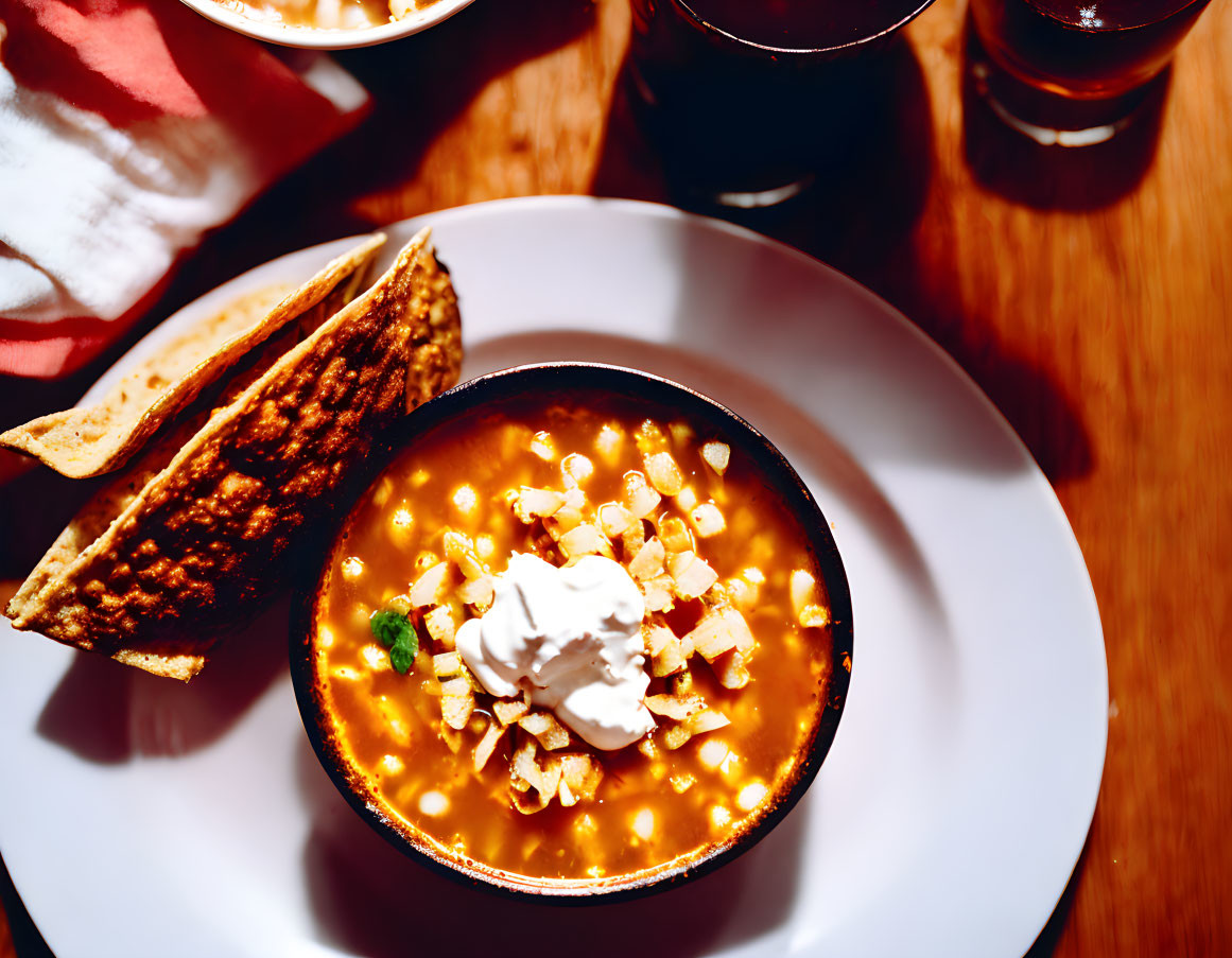 Savory soup with sour cream, croutons, bread, and drinks on wooden table