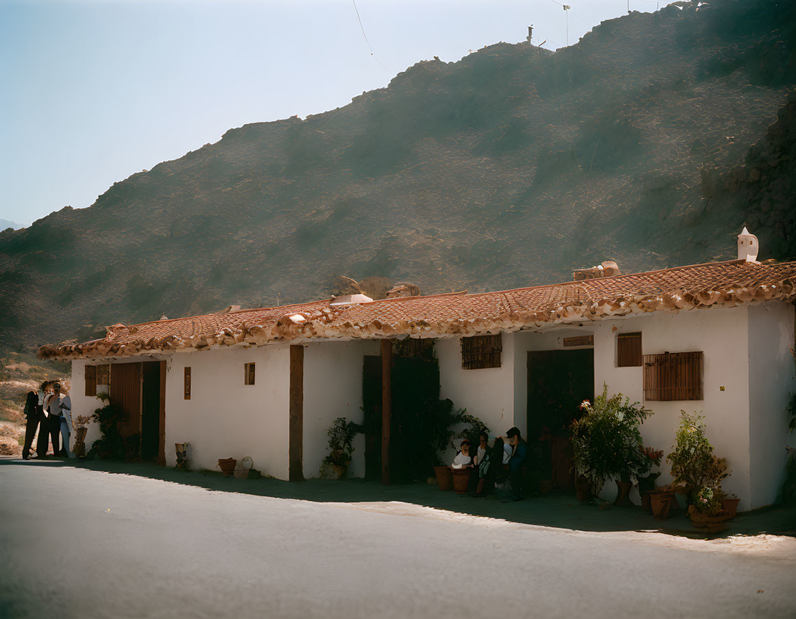 Group of people under white building porch with tiled roof and hills backdrop