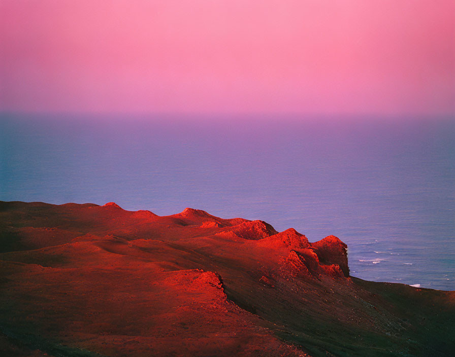 Coastal landscape at dusk: pink and purple hues, silhouetted hills, calm sea