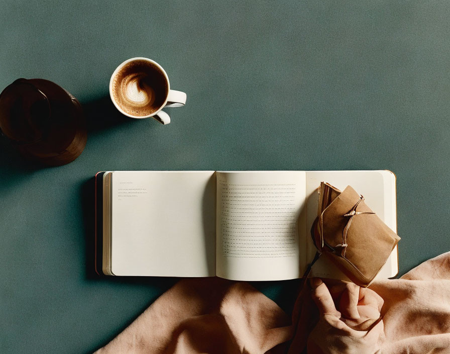 Open book on green surface with coffee, glasses, and hat - serene reading scene