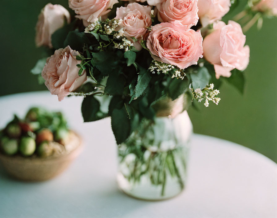 Pink roses bouquet in clear vase with green figs on white tabletop