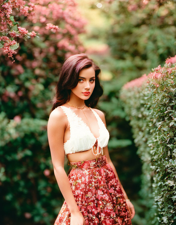 Woman in white crop top and floral skirt among pink flowers