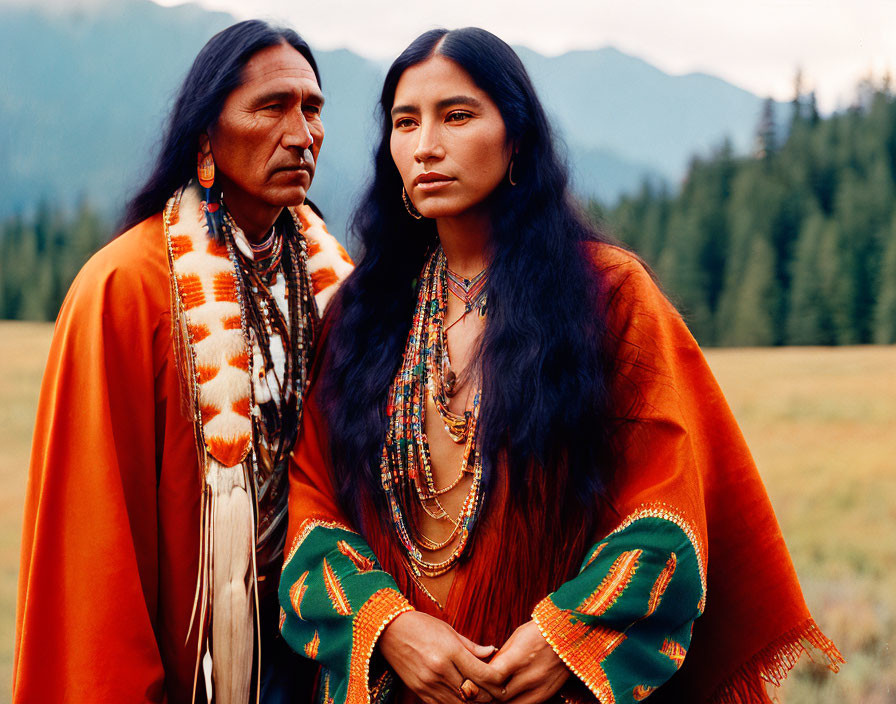 Native American individuals in traditional attire in grassy field with mountains