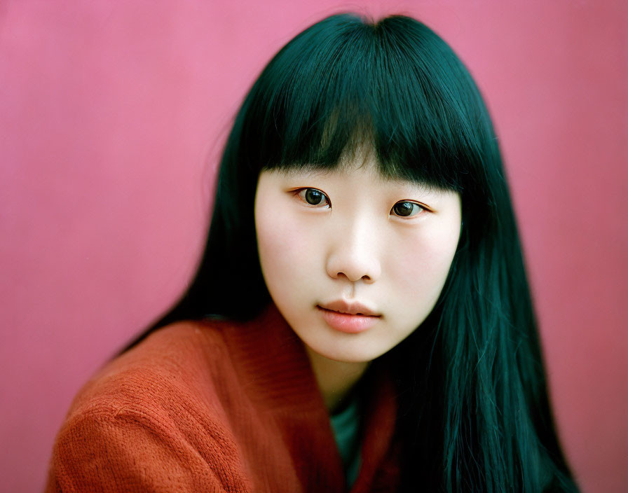 Young woman with long black hair in rust sweater on pink background