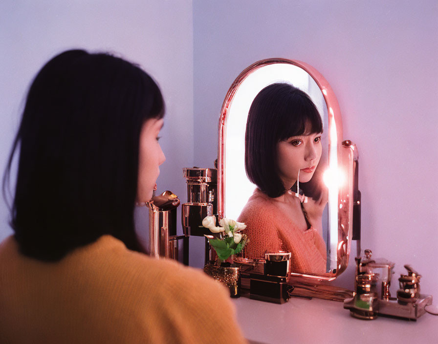 Woman in Yellow Top at Vanity with Makeup Items and Mirror with Lights