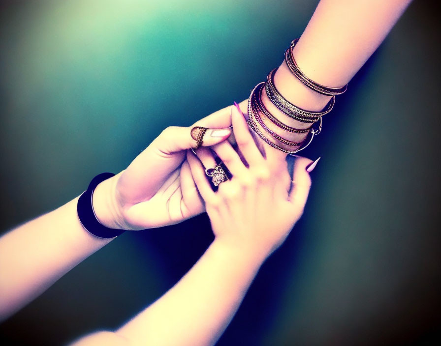 Hands holding each other with bracelets and rings.