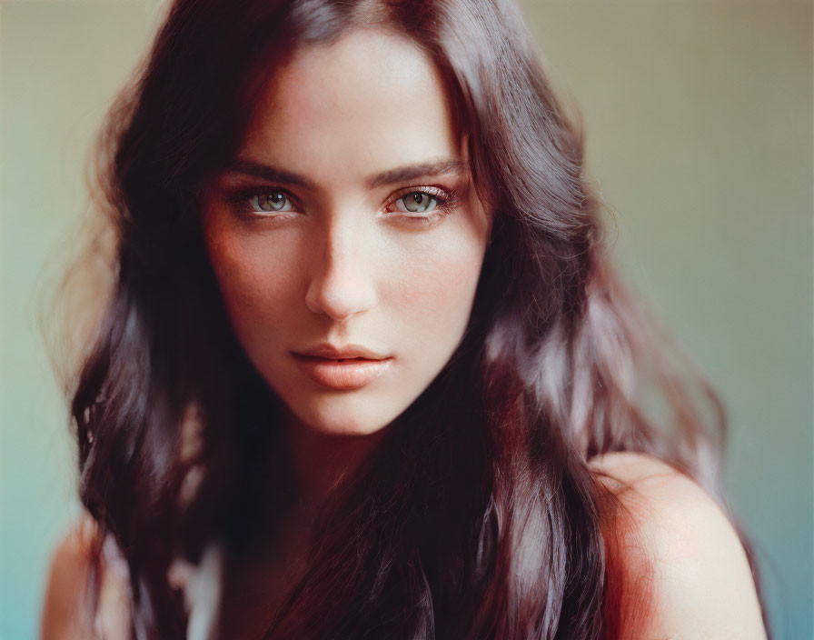 Portrait of woman with long dark hair and piercing green eyes against soft-focus background