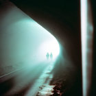 Silhouettes of two people at entrance of dimly lit tunnel with bright light.