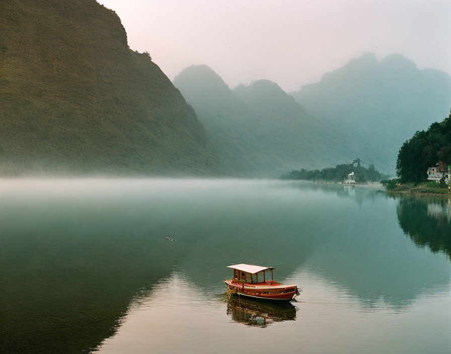 Misty river with boat surrounded by lush mountains