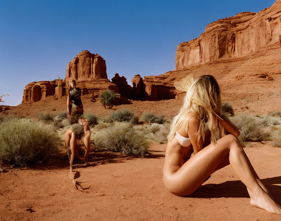 Three people in swimwear pose in desert with red sandstone formations