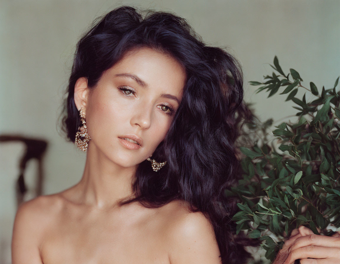 Dark-haired woman with earrings holding green plant on neutral background