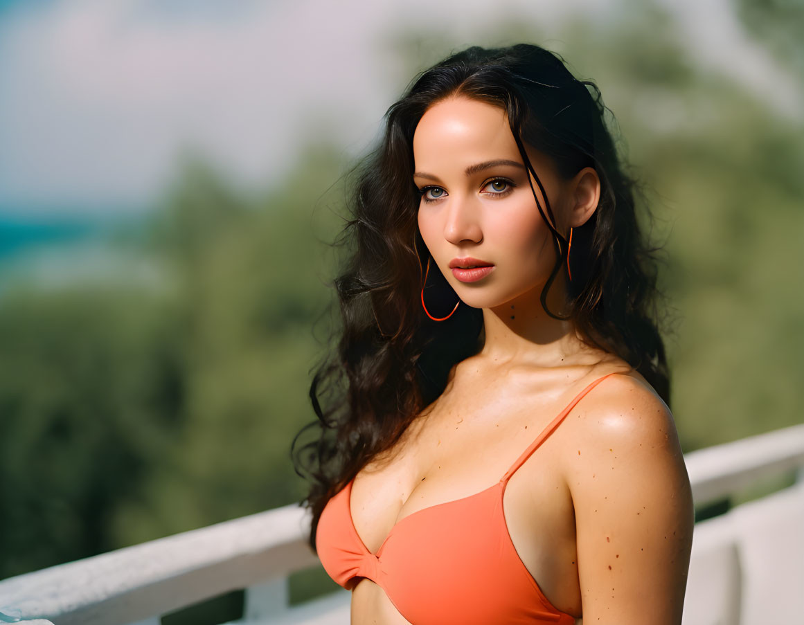 Dark-haired woman in orange bikini with hoop earrings in natural setting