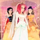 Three women in luxurious gowns and crowns on pink sparkly backdrop