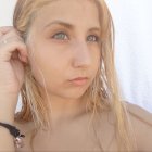 Blonde woman with braided hair and tattoo touching earring on white background