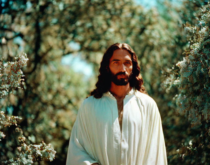 Bearded man in white robe amidst green foliage under blue sky