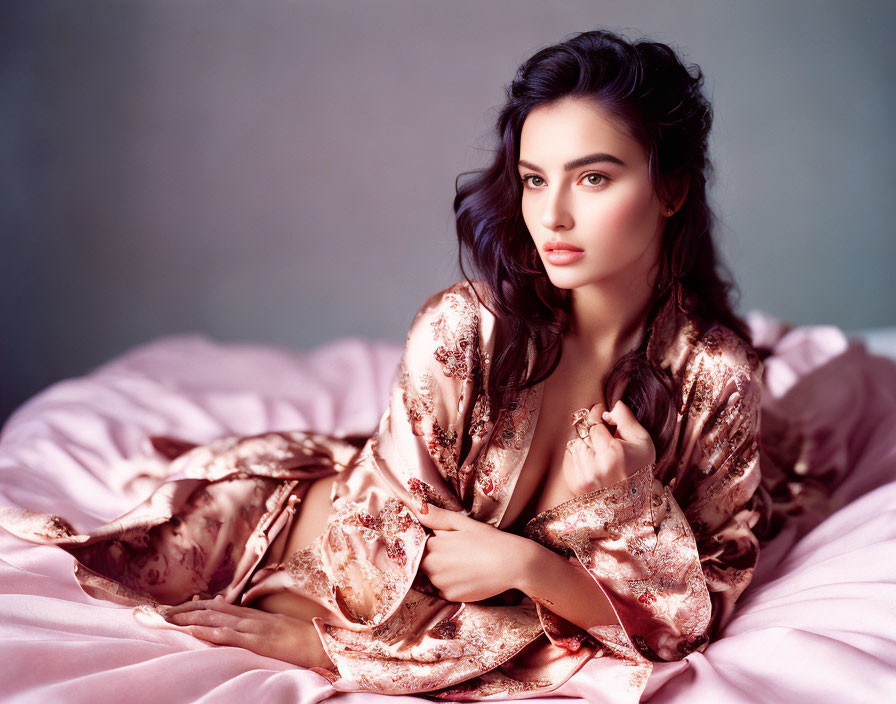 Woman in satin robe on bed with styled hair and subtle gaze.