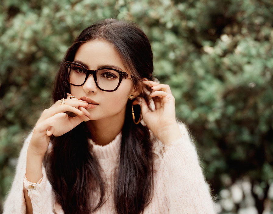 Woman with Glasses Holding Hair in Pink Sweater with Green Leaves Background