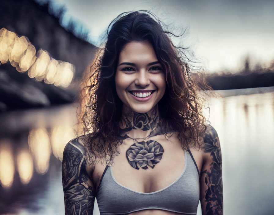 Smiling woman with tattoos standing outdoors near water and lights