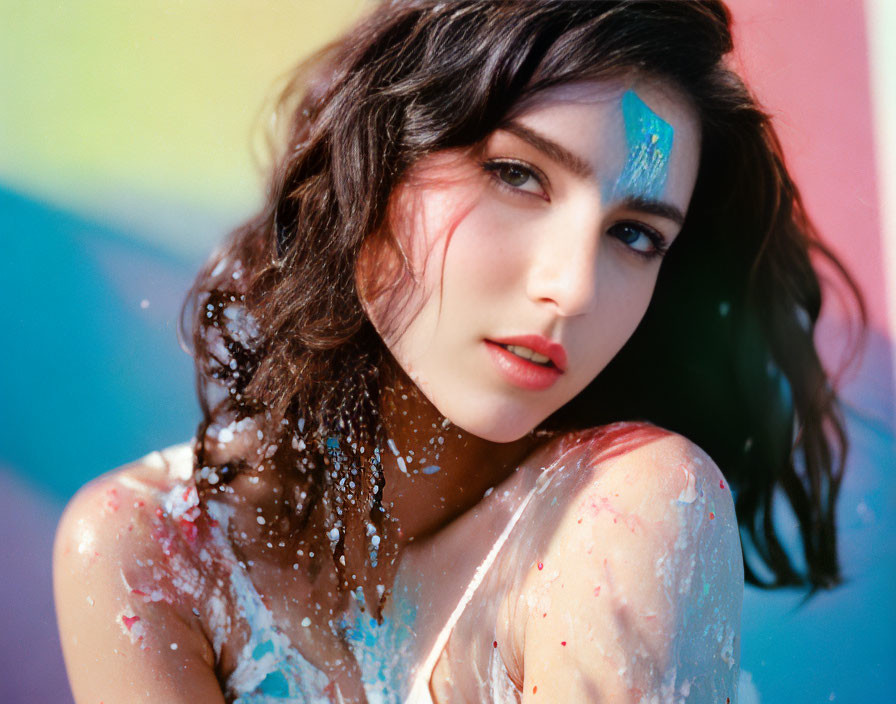 Young woman with paint splatters on skin in front of colorful background