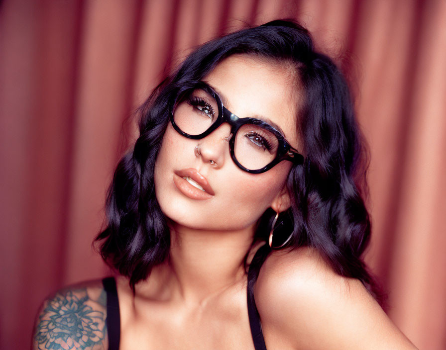 Woman with Black Framed Glasses and Shoulder Tattoo Poses Against Ruffled Curtain Backdrop