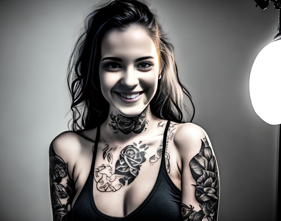 Smiling woman with tattoos in black tank top under studio light