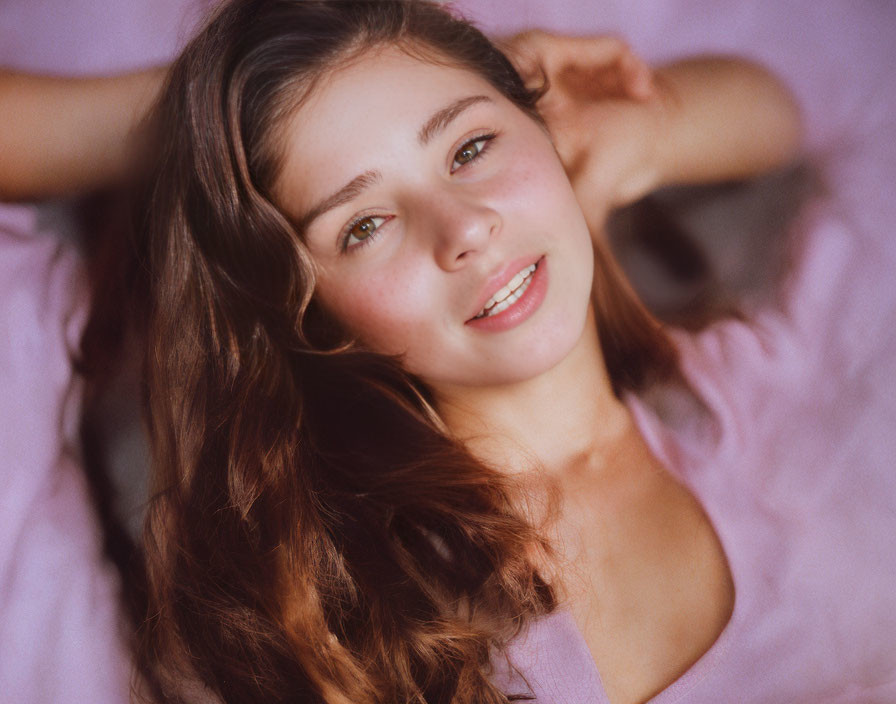 Young woman with flowing brown hair and gentle smile on pink backdrop