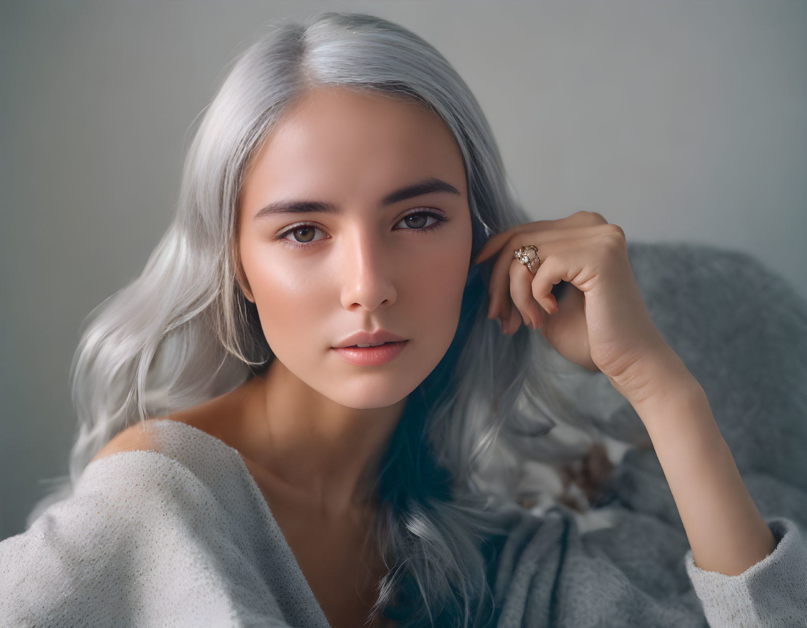 Silver-haired woman in serene pose with light sweater and ring against neutral backdrop