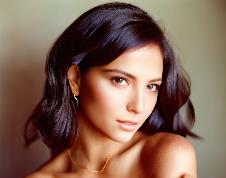 Dark-haired woman with soft makeup and bare shoulder in portrait against blurred background