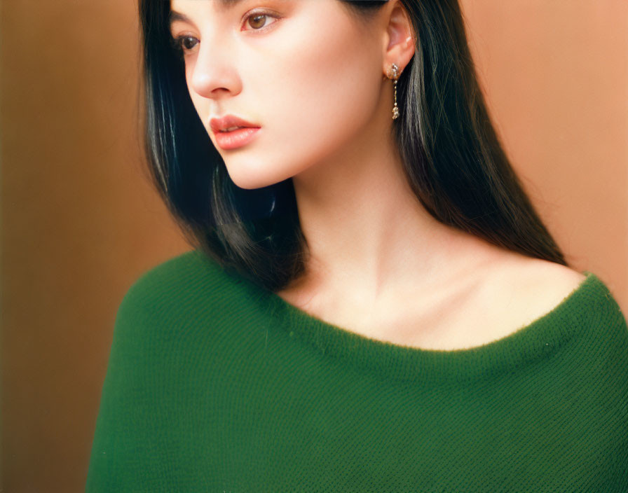 Woman with long dark hair in green sweater and earring gazes away.