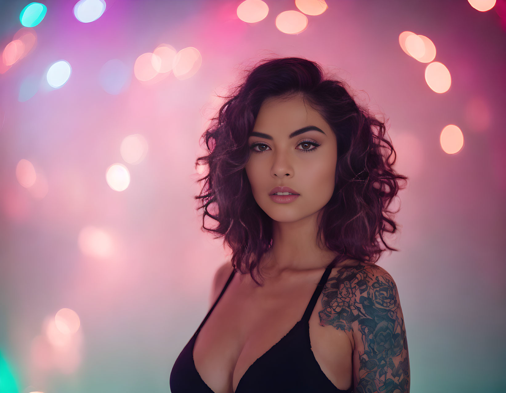 Tattooed woman with wavy hair in black top on colorful bokeh background