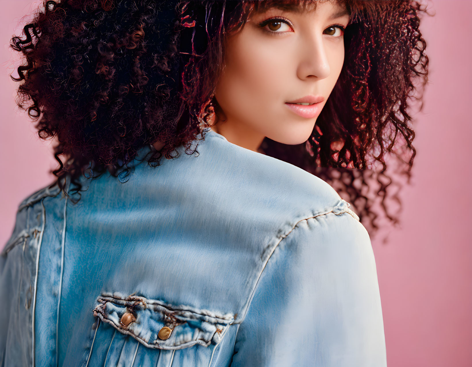 Curly-haired woman in denim jacket on pink background