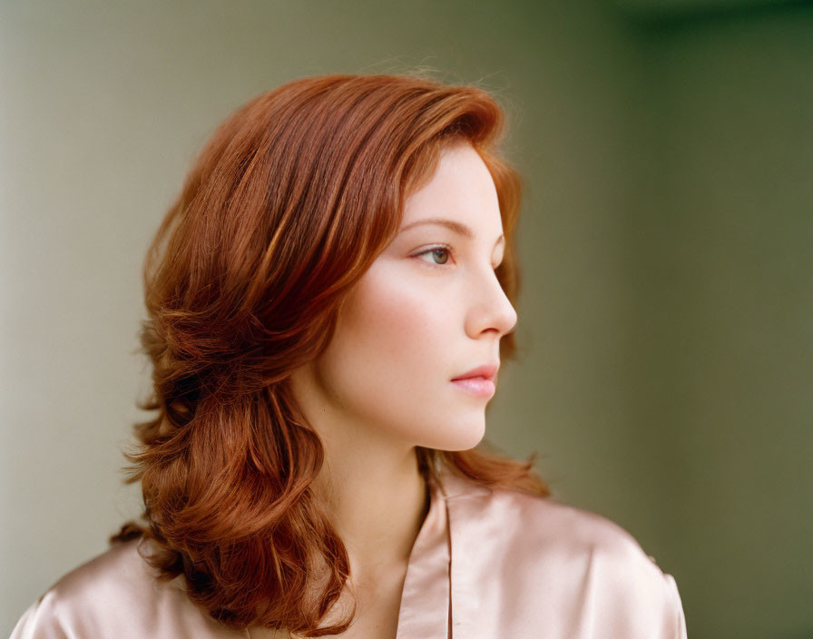 Auburn-haired woman in pink blouse against neutral background