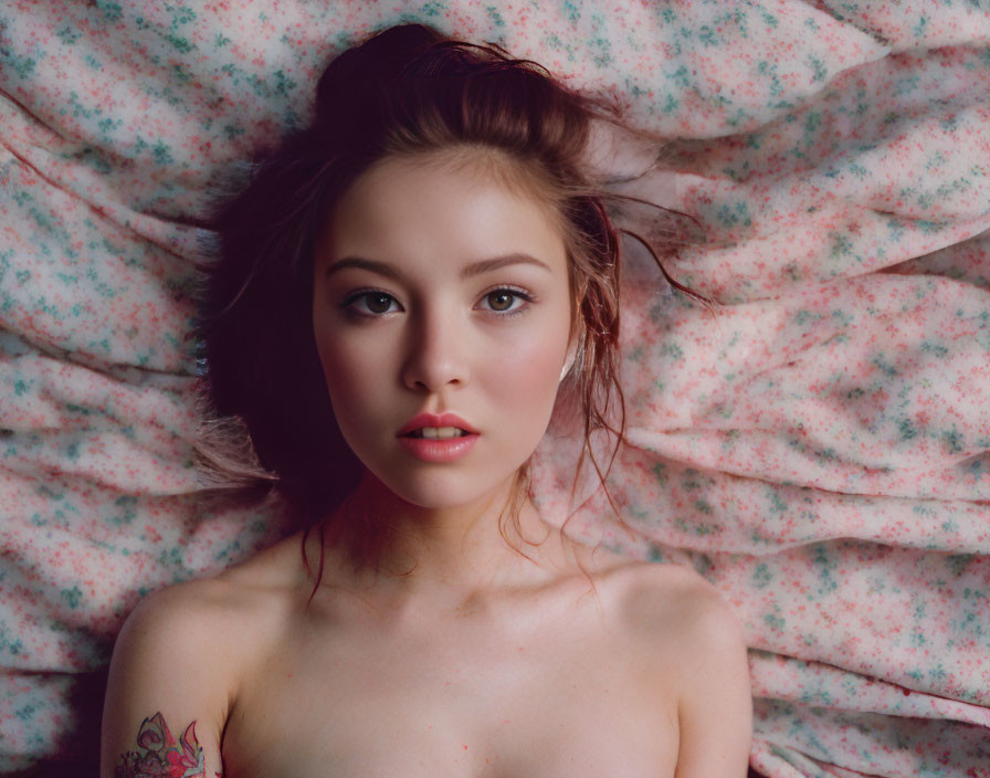 Young woman with subtle makeup and shoulder tattoo under floral sheet