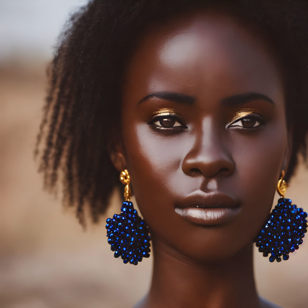 Portrait of Woman with Dark Skin, Gold Eyeshadow, and Blue Earrings