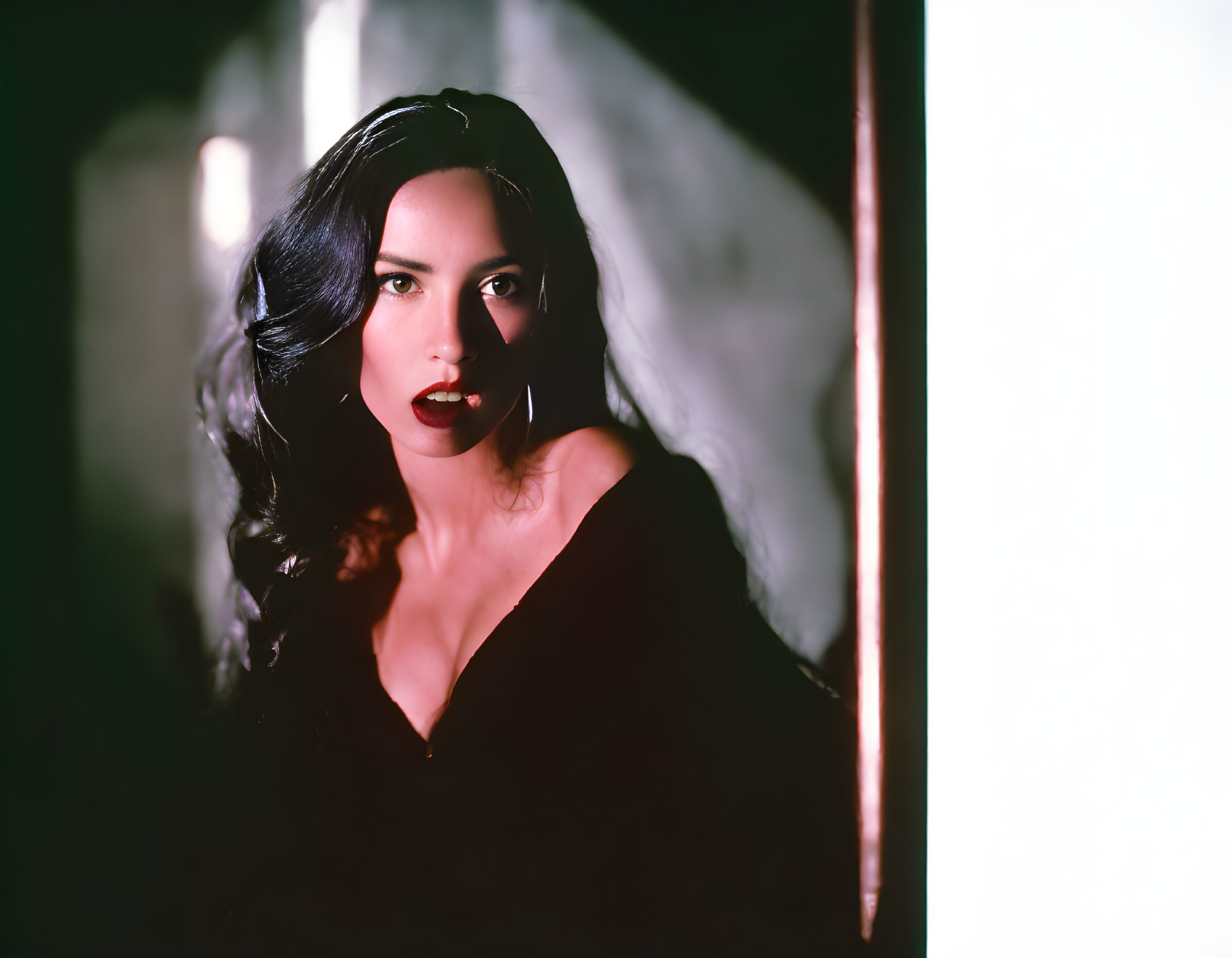 Dark-haired woman in black outfit with red lipstick under dramatic lighting