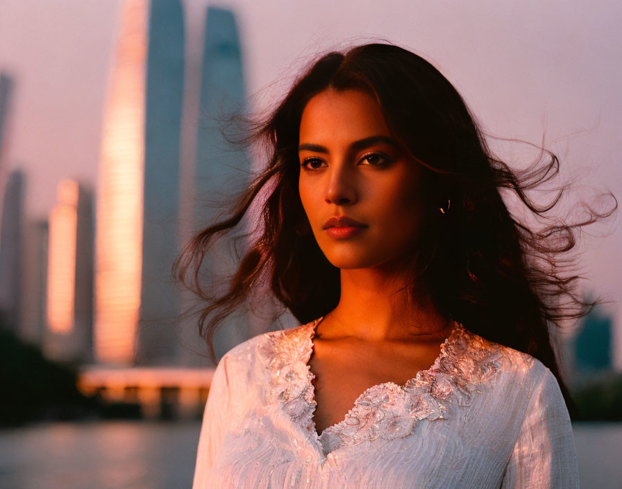 Dark-haired woman in white dress against blurred sunset skyline