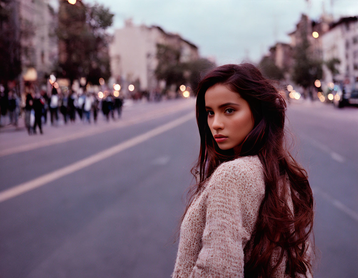 Woman looking back on city street at twilight with flowing hair and pedestrians.