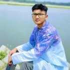 Stylish young boy in blue floral shirt sitting in field