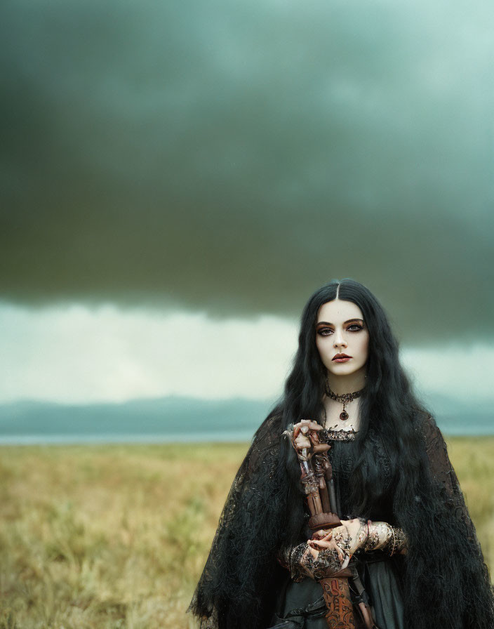 Gothic attire person with long dark hair in stormy field with staff