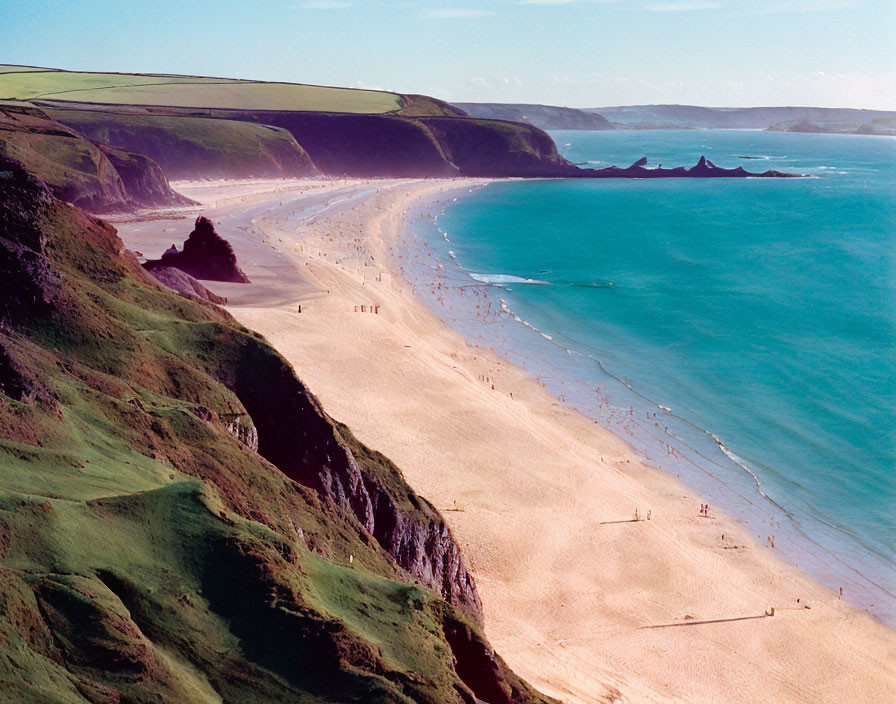 Sunlit beach with cliffs, people, and clear blue waters