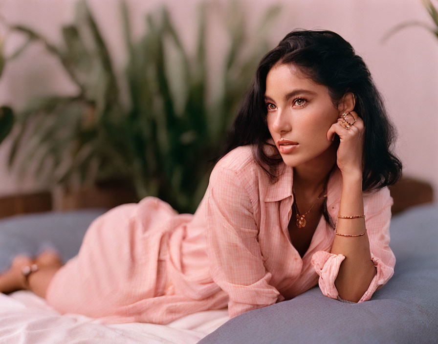 Pensive woman in pink outfit on blue surface with plants in background