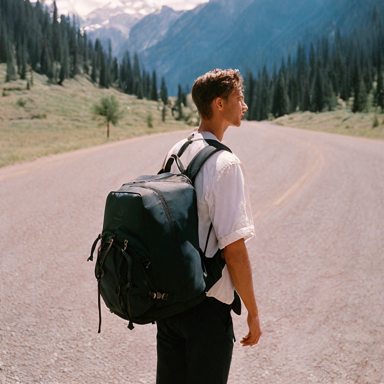 Man with backpack standing on road in nature, mountains in distance