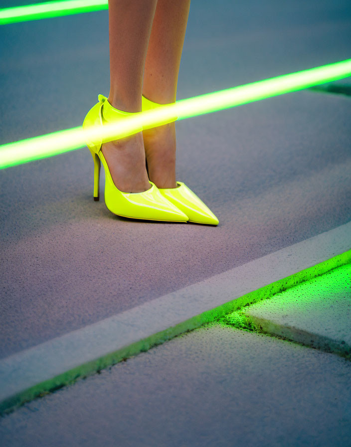 Vibrant yellow high-heeled shoes on pavement with neon green light strip