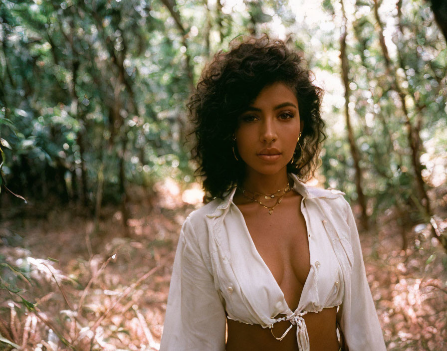 Curly-haired woman in white shirt and necklace in sunlit forest