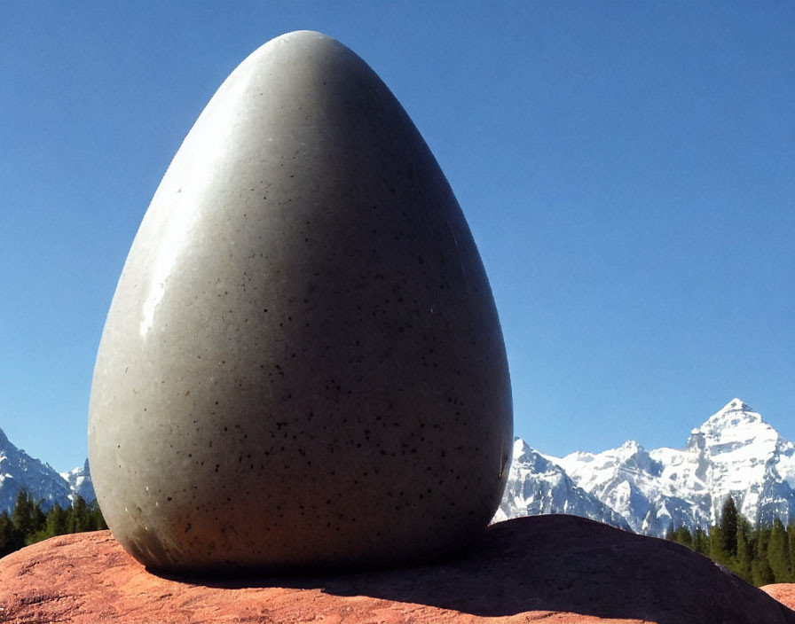 Egg-shaped stone sculpture against snowy mountains