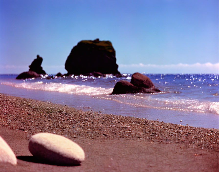 Tranquil beach scene with pebbles, waves, and rocks in clear sky