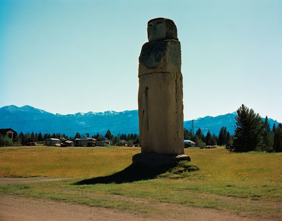 Moai statue in grassy field with mountains under clear sky