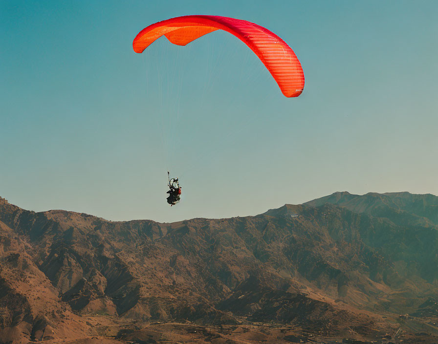 Vibrant orange paraglider soaring over mountainous terrain